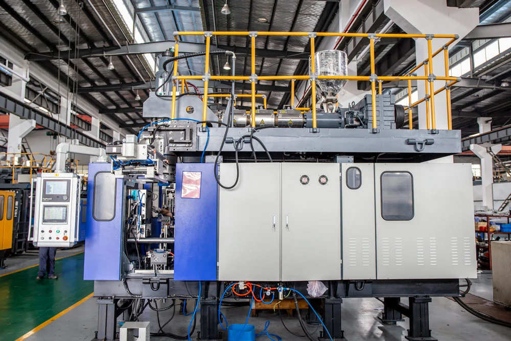 A large blue and white extrusion blow molding machine with a yellow service platform