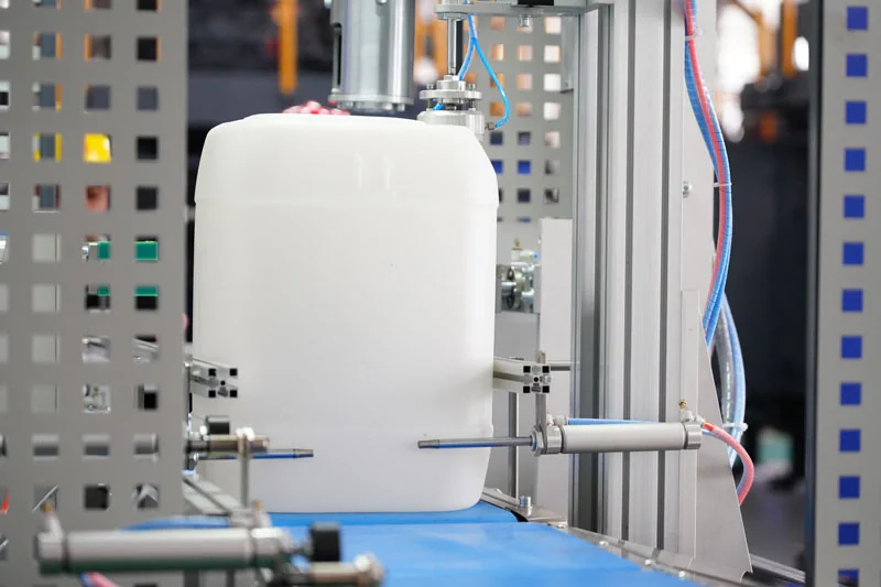 A white plastic jerry can between the handling equipment of a blow molding machine